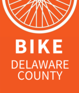 Orange logo for Bike Delco, 1/2 of a bike wheel and the words 'Bike Delaware County'